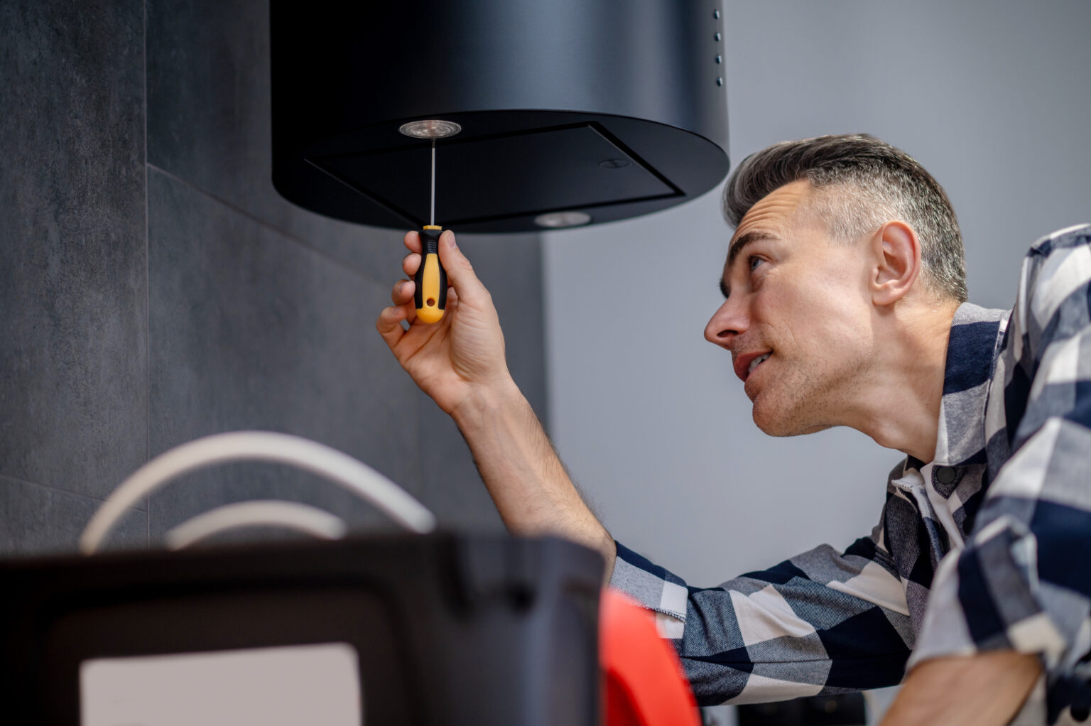 Backlight adjustment. Man with screwdriver carefully looking from below at kitchen hood hanging on wall twisting and adjusting lighting